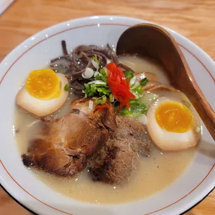 a bowl of ramen with boiled eggs and a wooden spoon