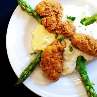 a plate of fried chicken with mashed potatoes and asparagus