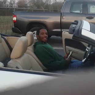 a man sitting in a convertible in a parking lot