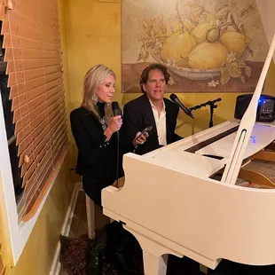 a man and a woman standing in front of a grand piano