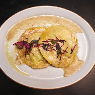 Two large, handmade ravioli stuffed with ricotta, spinach, an over-easy egg, in a brown butter truffle sauce