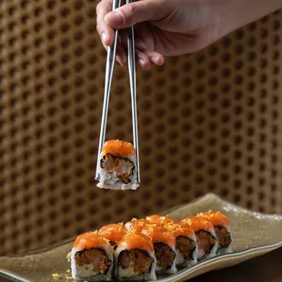 a person holding chopsticks over a plate of sushi