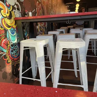 a row of white stools in front of a colorful mural