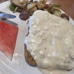 a plate of food with gravy, potatoes, and watermelon