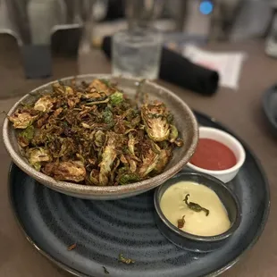 a bowl of fried brussels sprouts and sauces