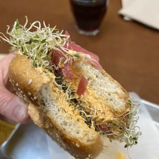 a person holding a sandwich with sprouts and ham