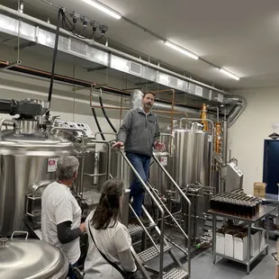 a man standing in front of a row of stainless steel tanks