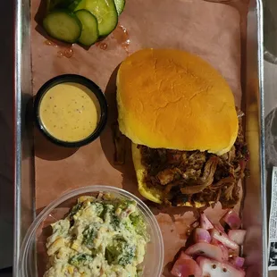 a tray of food including a pulled pork sandwich, coleslaw, and pickles