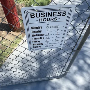 a business hours sign on a chain link fence