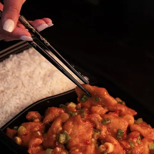  a person holding chopsticks over a container of food