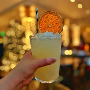 a person holding a drink with a slice of orange