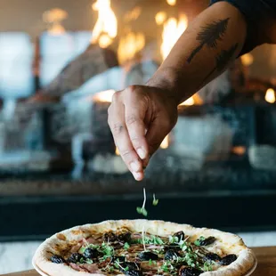 a hand sprinkling olives on a pizza