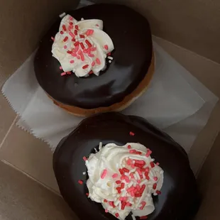 two chocolate donuts with white frosting and sprinkles