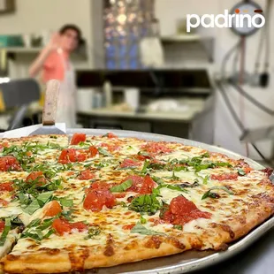 a pizza on a pan with a woman in the background