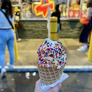 Vanilla soft serve with rainbow jimmies in a waffle cone