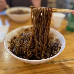 a person holding chopsticks over a bowl of noodles
