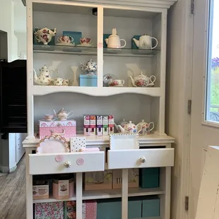 a white china cabinet with tea cups and teapots