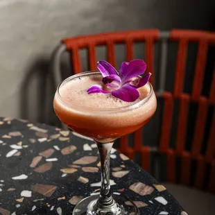 a cocktail with a purple flower on the rim