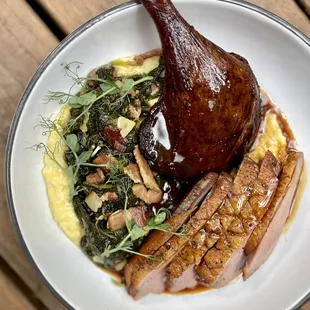 Grilled Duck a L&apos;Orange with sweet corn grits, smoked duck leg, and braised Southern greens.