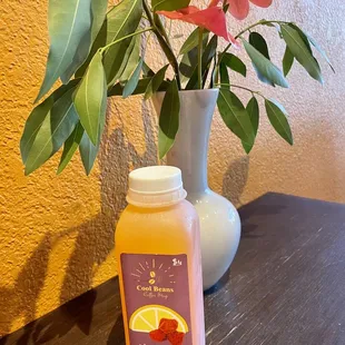 a bottle of orange juice next to a vase of flowers