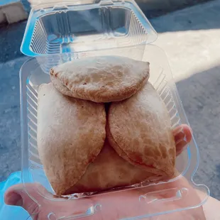 a hand holding a plastic container filled with pastries