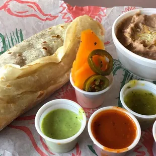 Fiesta burrito with a side of refried beans and an assortment of all the condiments