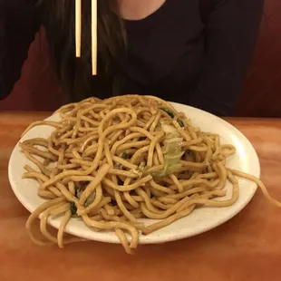 a woman holding chopsticks over a plate of noodles