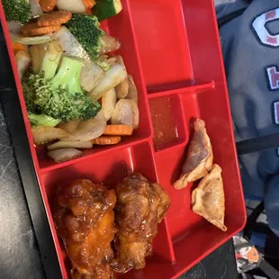 a red lunch tray with chicken, broccoli, and carrots