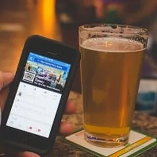 a person holding a cell phone and a glass of beer