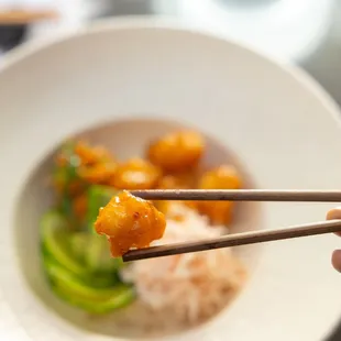 a person holding chopsticks over a bowl of food