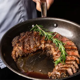 a person cooking steak in a skillet