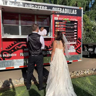 a bride and groom standing in front of a food truck