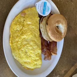 Ham and cheese omelette with a bagel and a side of bacon.