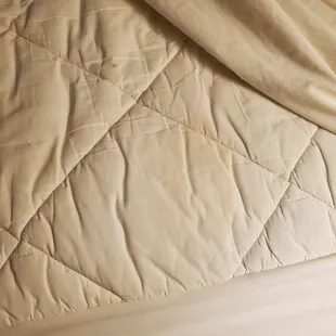 an unmade bed with a quilted cover