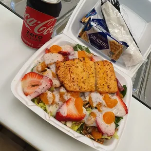 a plastic container with a salad and a can of soda