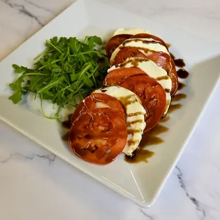 Caprese salad: Layered Roma tomatoes, Belgioioso mozzarella, and arugula drizzled with balsamic glaze and olive oil