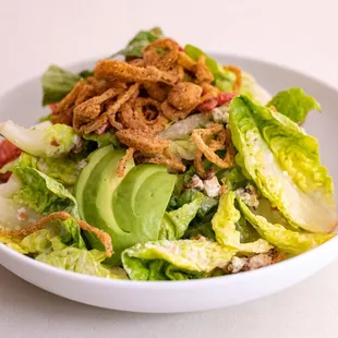 a salad with lettuce, avocado, and fried onions