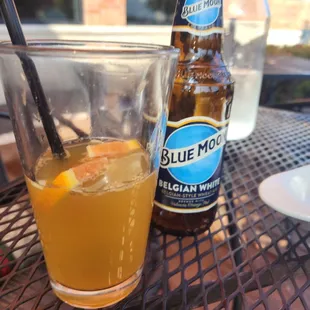 a glass of orange juice and a bottle of blue moon