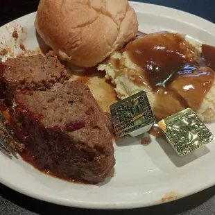Meatloaf with mashed potatoes and brown gravy and a dinner roll as well as another side of your choice.