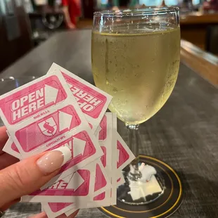 a person holding a glass of wine and a pack of tickets