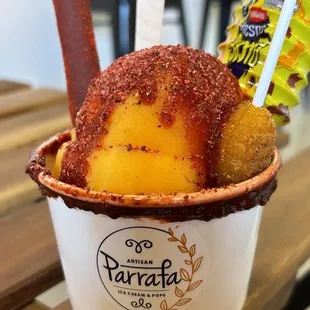 Two scoops of ice cream. Mango seen in top, with chango, Tajín, a lollipop, and Lucas.