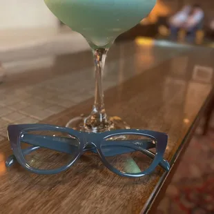 a glass of blue liquid and a pair of glasses