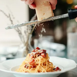 someone grating cheese over a plate of spaghetti
