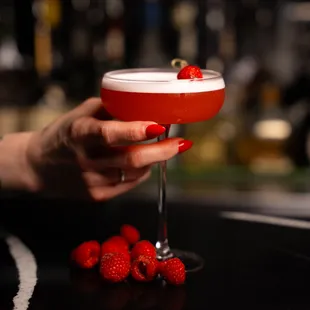 a hand holding a red cocktail with strawberries