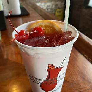 a drink in a plastic cup with a straw and a cherry garnish