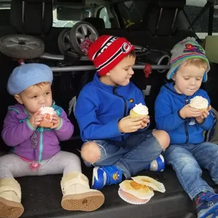 three children sitting in the back of a car eating hotdogs