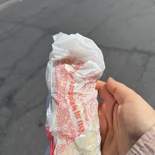 a person holding a sandwich wrapped in plastic