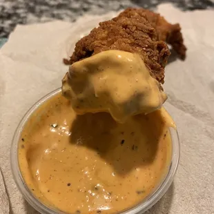 a piece of fried chicken being dipped with cheese sauce