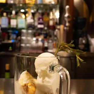 a glass of ice cream with a sprig of rosemary