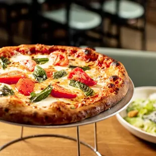a pizza on a plate with a salad in the background